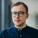 Portrét Martina Dvořáka, muže s krátkými vlasy, brýlemi a modrou košilí, s pohledem upřeným vpřed.