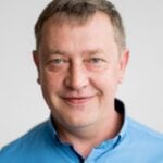 Portrét usmívajícího se muže středního věku s krátkými, světle hnědými vlasy v modré košili.