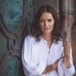 A woman in a flowing white dress stands serenely before an ornate, ancient-looking door, embodying grace and inner peace.