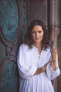 A woman in a flowing white dress stands serenely before an ornate, ancient-looking door, embodying grace and inner peace.